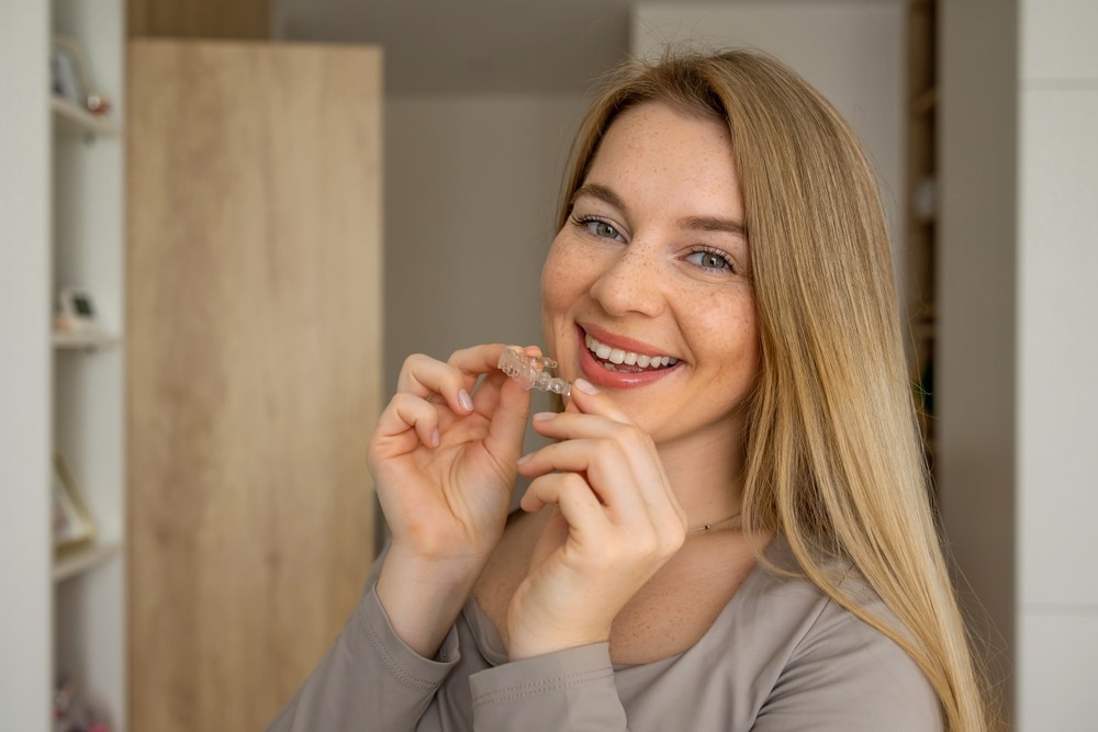 Pretty young woman holds a clear aligner and smiles brightly in Hot Springs