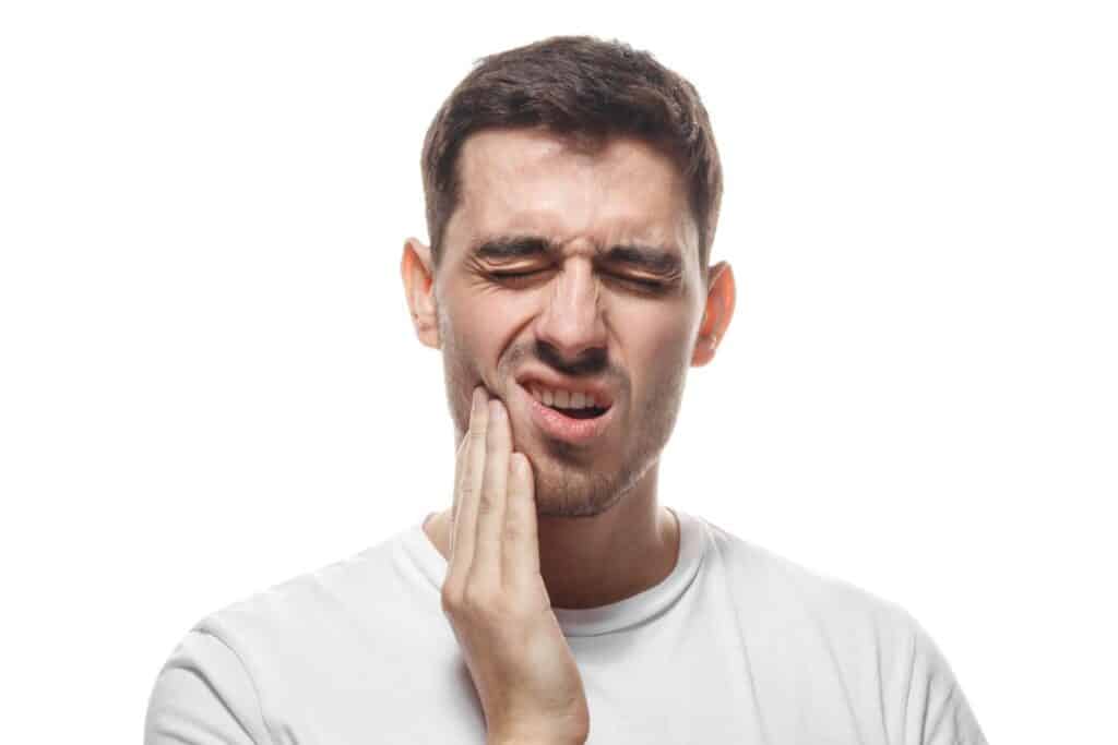 Man wincing and grabbing at his jaw in pain from a wisdom tooth that needs to be extracted. Man wincing and grabbing at his jaw in pain from a wisdom tooth that needs to be extracted.
