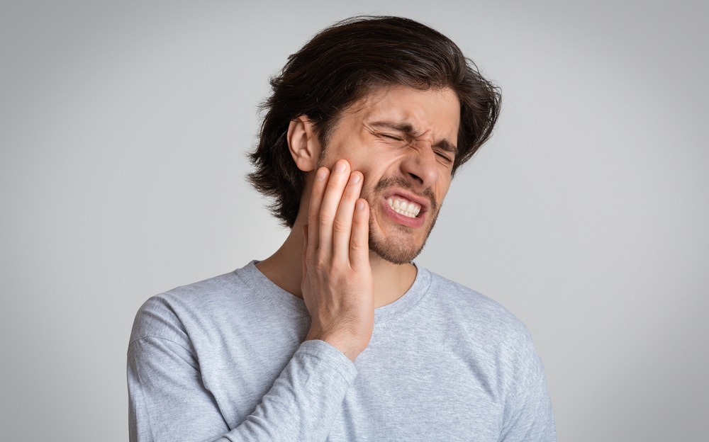 Man clutching his mouth in pain from an emergency dental problem issue, in need of care.